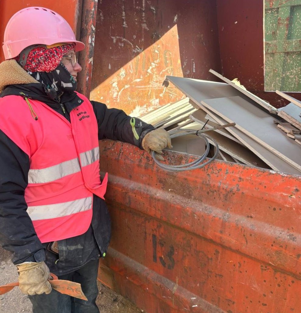 Ressourcekoordinator i pink hjelm ved en container